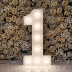 May include: A large, white, freestanding marquee number one featuring eight evenly spaced, circular, illuminated light bulbs along its front face. The structure has a clean, matte finish and a power cord extending from the base.