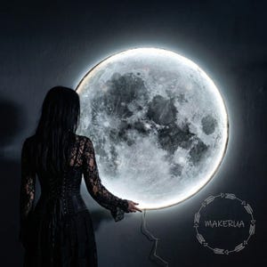 以下が含まれることがあります： 詳細な月の表面を持つ、大きな、照らされた月の壁の芸術作品。月は明るく光るハローに囲まれています。黒いレースのドレスを着た人が月の近くに立っています。Makeruaのロゴが右下にあります。
