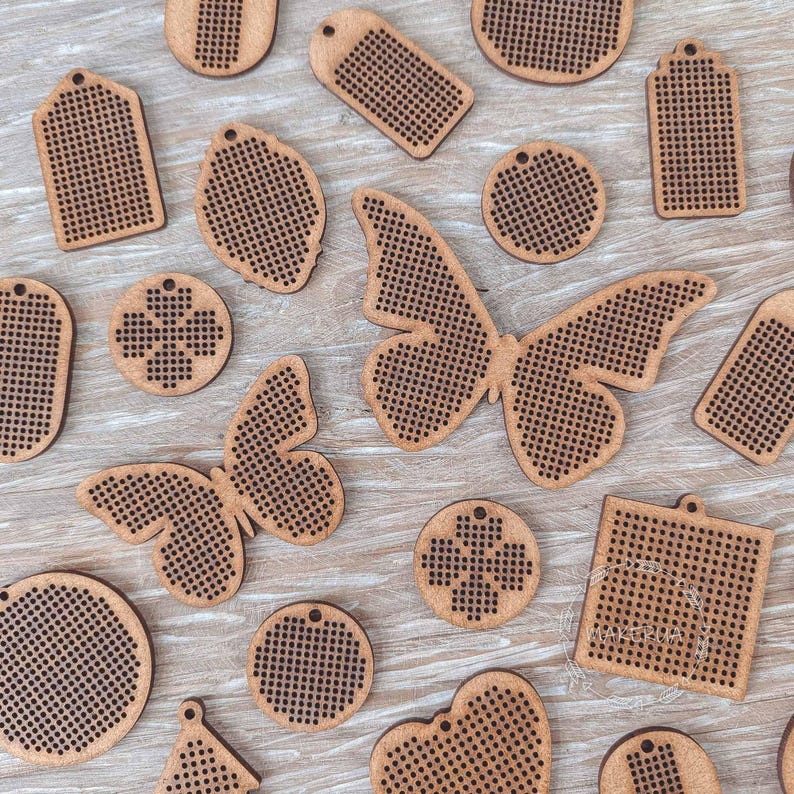 K&ouml;nnte beinhalten: Eine Sammlung von Holzformen f&uuml;r Bastelarbeiten, darunter Schmetterlinge, Anh&auml;nger, Kreise und andere geometrische Formen. Jedes St&uuml;ck ist hellbraun mit einem perforierten Gittermuster, ideal f&uuml;r Kreuzstich- oder Stickprojekte. Die Formen liegen auf einer hellen Holzoberfl&auml;che.