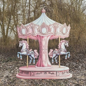 Può includere: Una giostra rosa e bianca con due figure di unicorni. La giostra ha una tettoia e una base decorative, con pali di supporto dorati. Gli unicorni sono bianchi con zoccoli blu e criniere rosa. Sfondo naturale.
