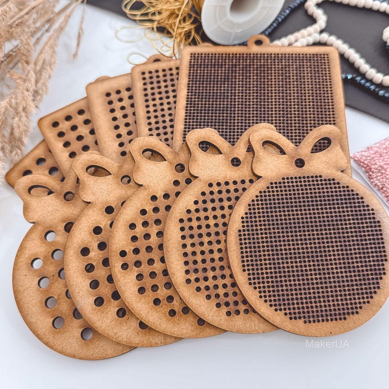 K&ouml;nnte beinhalten: Eine Sammlung unfertiger Holzornamente und quadratischer Formen mit perforierten L&ouml;chern zum Basteln. Die Ornamente sind wie Weihnachtskugeln mit einer Schleife oben geformt. Die quadratischen Formen haben eine Schlaufe zum Aufh&auml;ngen. Das Holz hat eine nat&uuml;rliche, hellbraune Farbe.