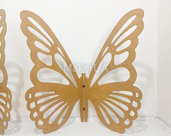 May include: A large, laser-cut butterfly decoration made of light brown wood. The butterfly has intricate wing details with open spaces, and the text "MakerUA" is visible on the body. The wings are symmetrical, and the overall design is suitable for wall decor.