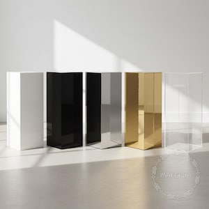 Könnte beinhalten: Eine Reihe von sechs Präsentationspodesten in verschiedenen Farben: Weiß, Schwarz, Silber, Gold und transparent. Die Podeste sind rechteckig und haben eine glänzende Oberfläche. Das transparente Podest ist durchsichtig. Das Makerua-Logo befindet sich unten rechts.