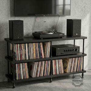 May include: A black, three-tiered media console with a record player, amplifier, and speakers. The shelves are filled with vinyl records. The console has a dark finish and is set against a grey wall.