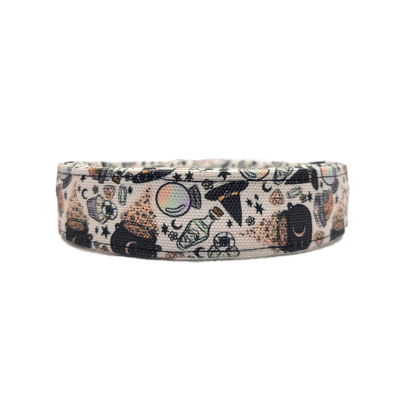 Puede incluir: Un collar para perros beige con un patr&oacute;n repetido de ilustraciones con tem&aacute;tica de brujas. El dise&ntilde;o incluye calderos, botellas de pociones, bolas de cristal, sombreros de bruja y estrellas. El collar est&aacute; hecho de una tela resistente.