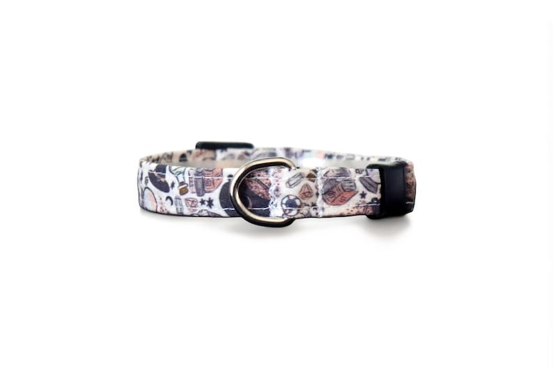 Puede incluir: Collar para perros con un patr&oacute;n de objetos marrones, negros y azules sobre un fondo blanco. Tiene una anilla en D de metal plateado y una hebilla de pl&aacute;stico negro. El collar est&aacute; dise&ntilde;ado para mascotas.
