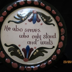 Puede incluir: Plato decorativo redondo de cerámica con la cita "He also serves who only stand and waits". El plato tiene un centro blanco con texto marrón y diseños florales en azul, rojo y verde. El borde es negro con puntos rojos.