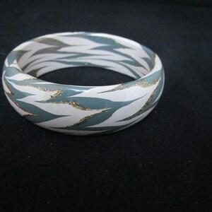 May include: White and teal bangle bracelet with a gold glitter pattern.