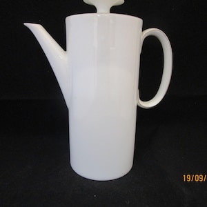 May include: White ceramic coffee pot with a lid and a handle. The pot has a simple, modern design.