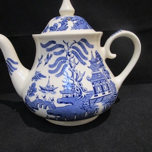 May include: A white teapot with a blue and white willow pattern. The teapot has a lid and a handle.