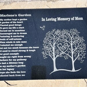 May include: Black granite memorial plaque with a poem about a mother's garden and a white silhouette of two trees with a heart shape in the center. The text reads "Marlene's Garden" and "In Loving Memory of Mom".
