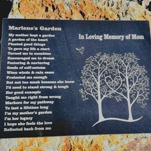 May include: A black granite memorial plaque with a poem titled "Marlene's Garden" and the words "In Loving Memory of Mom". The poem is about a mother's love and the lessons she taught her child. The plaque features two stylized trees with a heart shape in the center.
