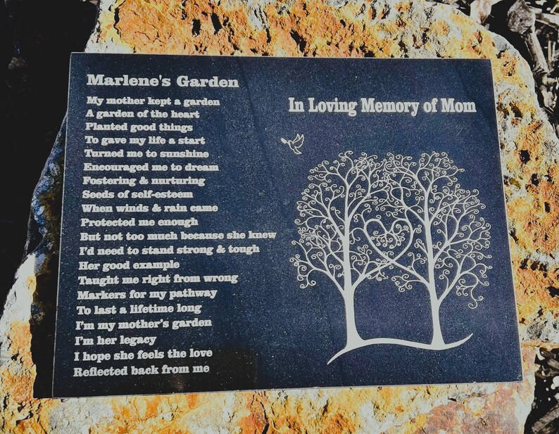 May include: A black granite memorial plaque with a poem titled "Marlene's Garden" and the words "In Loving Memory of Mom". The poem is about a mother's love and the lessons she taught her child. The plaque features two stylized trees with a heart shape in the center.