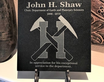 May include: Black granite plaque with a silver inscription honoring John H. Shaw, Chair, Department of Earth and Planetary Sciences, 2006-2019. The plaque features a silver crossed pickaxe design and the text "In appreciation for his exceptional service to the department."