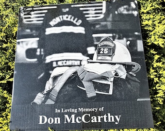 May include: Black and white photo memorial plaque with the text "In Loving Memory of Don McCarthy". The plaque features a firefighter's helmet with the words "Monticello Chief 25" on it.