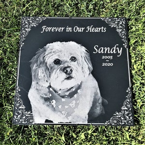 May include: Black granite pet memorial with a white dog etched in the center. The inscription reads "Forever in Our Hearts" and "Sandy 2005 - 2020".