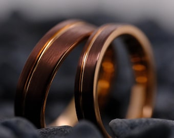 May include: Two rings with a brushed dark brown finish and a polished rose gold centre groove. The bands feature a smooth, rounded profile with a metallic sheen, showcasing a distinct contrast between the matte outer surface and the reflective inner line.