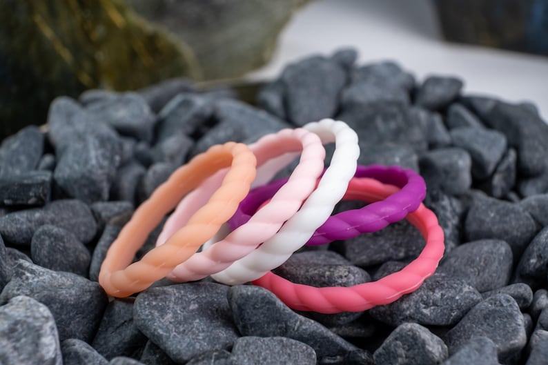 2mm braided silicone activity bands in white, pink, baby pink,hot pink, and purple, on top of a bed of grey stones.