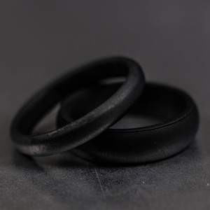 4 and 6mm black silicone bands unisex laying on each other with a dark background.