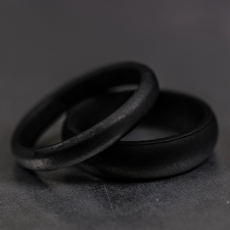 4 and 6mm black silicone bands unisex laying on each other with a dark background.