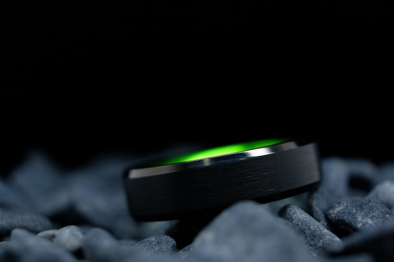 6mm brushed black tungsten carbide wedding band with high gloss green interior on a bed of grey stones.