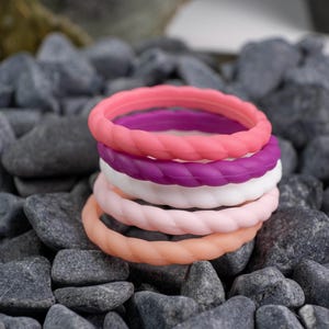2mm braided silicone activity bands in white, pink, baby pink,hot pink, and purple, on top of a bed of grey stones.