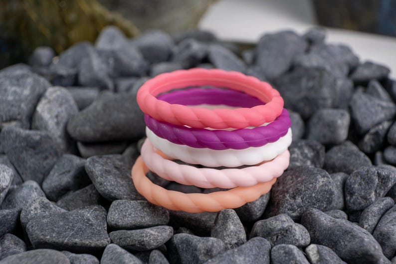 2mm braided silicone activity bands in white, pink, baby pink,hot pink, and purple, on top of a bed of grey stones.