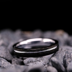 4mm black hammered tungsten carbide wedding band with a silver stripe and interior on a bed of grey stones.