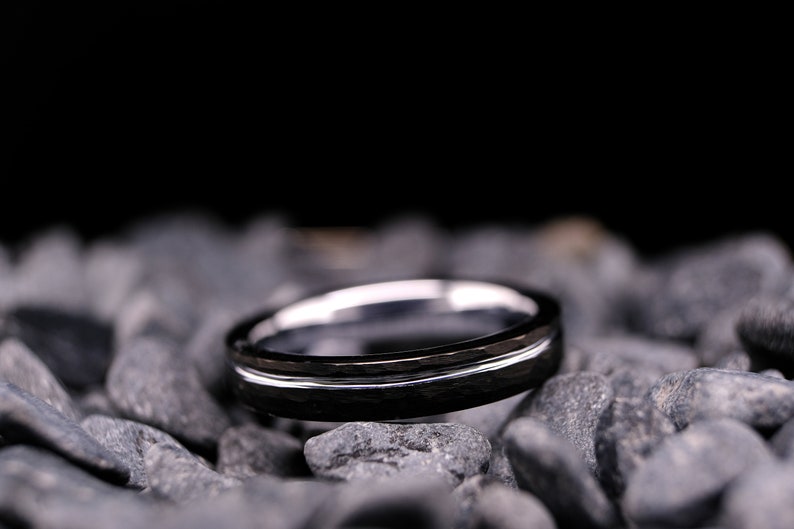 4mm black hammered tungsten carbide wedding band with a silver stripe and interior on a bed of grey stones.