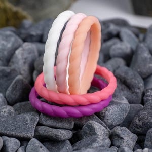 2mm braided silicone activity bands in white, pink, baby pink,hot pink, and purple, on top of a bed of grey stones.