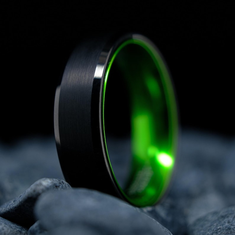 6mm brushed black tungsten carbide wedding band with high gloss green interior on a bed of grey stones.