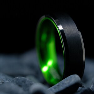 6mm brushed black tungsten carbide wedding band with high gloss green interior on a bed of grey stones.