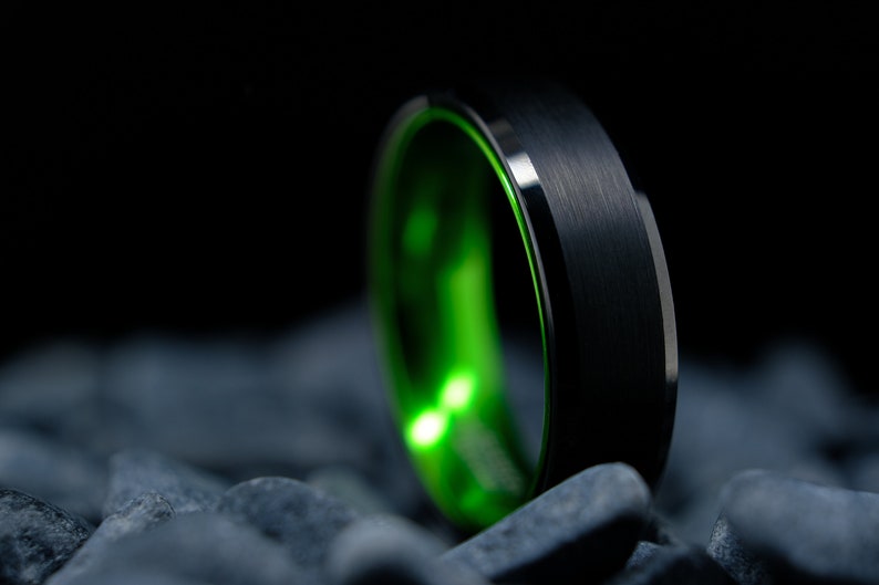 6mm brushed black tungsten carbide wedding band with high gloss green interior on a bed of grey stones.