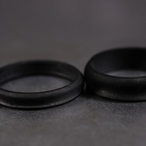 4 and 6mm black silicone bands unisex laying on each other with a dark background.