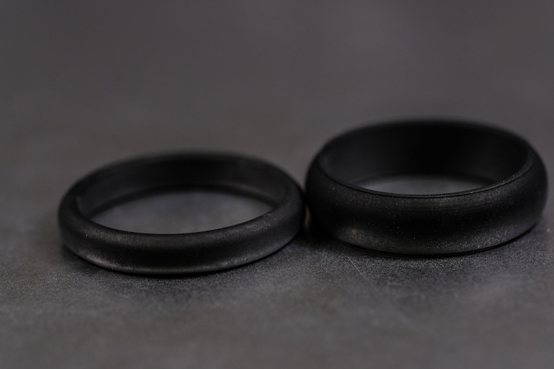4 and 6mm black silicone bands unisex laying on each other with a dark background.