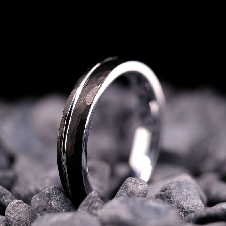 4mm black hammered tungsten carbide wedding band with a silver stripe and interior on a bed of grey stones.