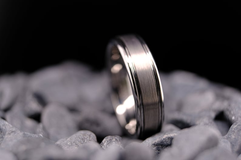 6mm brushed silver tungsten carbide wedding band with polished side walls on a bed of grey stones.