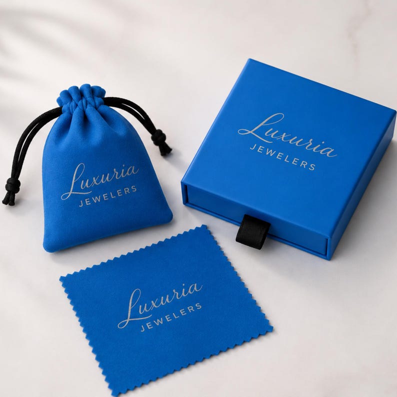 May include: A blue jewelry box, drawstring pouch, and cleaning cloth. The box and pouch have the text "Luxuria Jewelers" in silver script. The drawstring on the pouch is black.