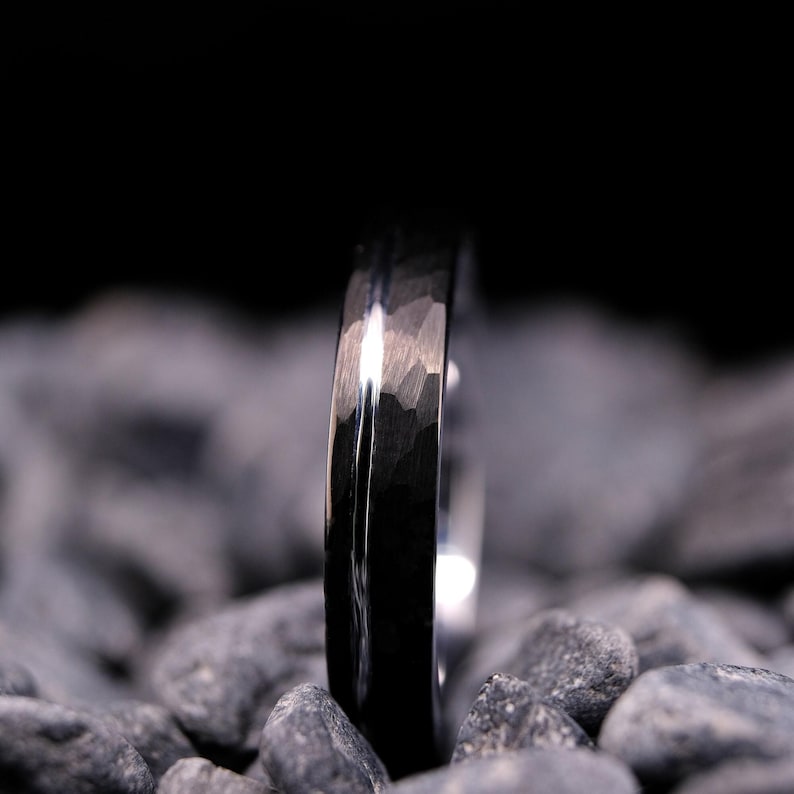 4mm black hammered tungsten carbide wedding band with a silver stripe and interior on a bed of grey stones.
