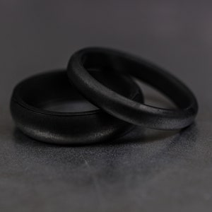 4 and 6mm black silicone bands unisex laying on each other with a dark background.