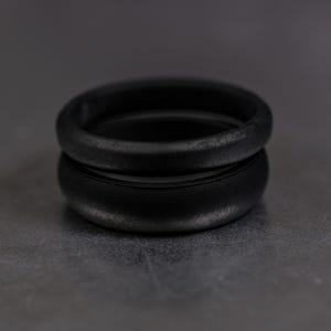 4 and 6mm black silicone bands unisex laying on each other with a dark background.