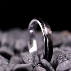 4mm black hammered tungsten carbide wedding band with a silver stripe and interior on a bed of grey stones.