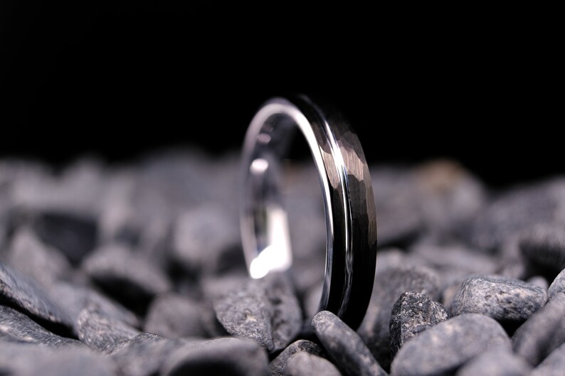 4mm black hammered tungsten carbide wedding band with a silver stripe and interior on a bed of grey stones.