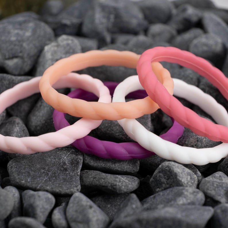 2mm braided silicone activity bands in white, pink, baby pink,hot pink, and purple, on top of a bed of grey stones.