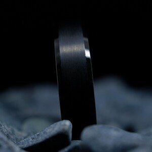 6mm brushed black tungsten carbide wedding band with high gloss green interior on a bed of grey stones.
