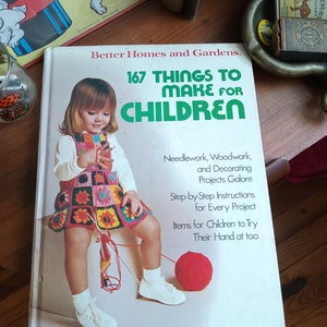 May include: A vintage book titled "167 Things to Make for Children" with a young girl on the cover wearing a colorful crocheted dress and holding yarn. The book features needlework, woodworking, and decorating projects.
