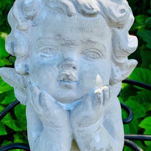 May include: A white ceramic cherub planter with a sweet expression, holding its hands together under its chin. The planter has a slightly distressed finish and is perfect for adding a touch of whimsy to your home decor.