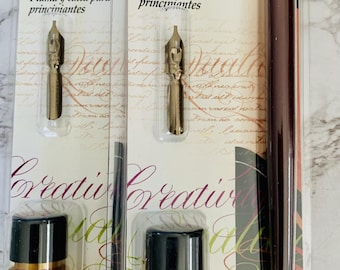 Könnte beinhalten: Ein Kalligrafie-Set mit zwei Federhaltern, zwei Flaschen Goldtinte und einem burgunderfarbenen Federhalter. Die Verpackung zeigt den Text "Manuscript Leonardt Beginners dip pen & ink set" in Weiß auf schwarzem Hintergrund. Der Text "Plume et encre pour débutants" und "Pluma y tinta para principiantes" ist ebenfalls in Französisch und Spanisch enthalten.