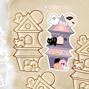 May include: A Halloween-themed cookie cutter set featuring a haunted house design with a ghost, cat, and pumpkins. The cookie cutter is made of a light brown material and is designed to cut out the shape of a spooky house.
