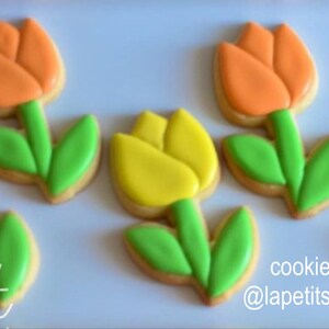 Op de afbeelding: Vijf gedecoreerde suikerkoekjes in de vorm van tulpen. De koekjes zijn versierd met roze, oranje en gele glazuur. De bladeren zijn groen. De tekst "La Petite Sweet" staat in de linkerbenedenhoek van de afbeelding. De tekst "cookies by @lapetitsweet.cl" staat in de rechterbenedenhoek van de afbeelding.